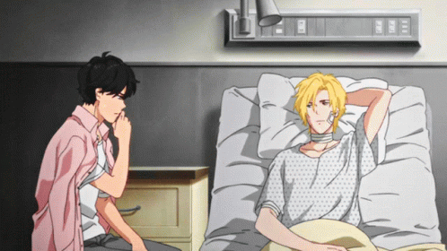a man in a pink shirt sits next to another man in a hospital bed