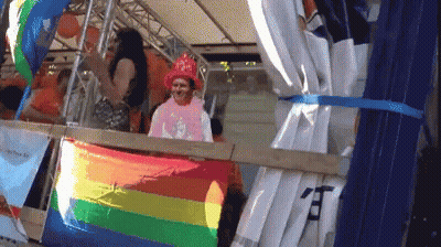 A Man In A Pink Shirt Stands Behind A Rainbow Flag With Chinese Characters On It GIF