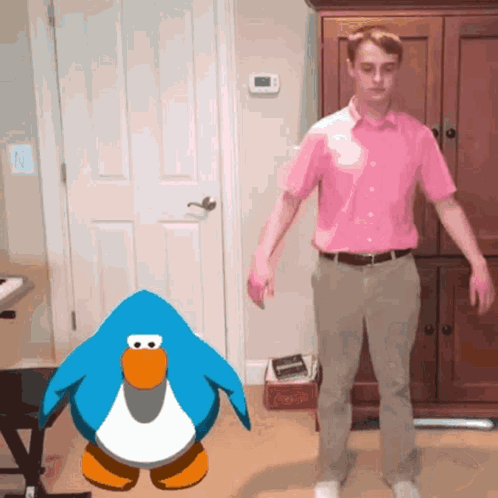 A Man In A Pink Shirt Stands In Front Of A Penguin GIF