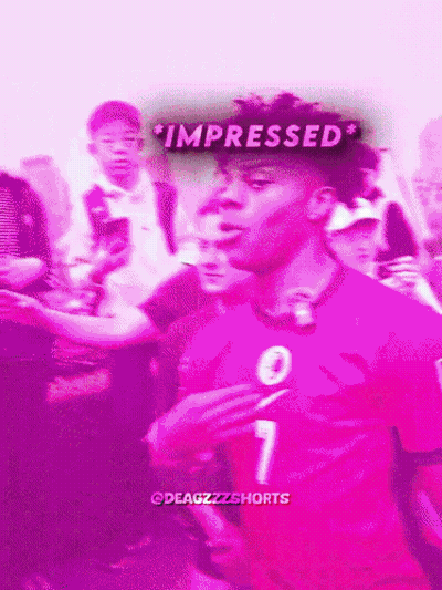 A Man In A Pink Shirt With The Number 7 On It Stands In Front Of A Crowd GIF