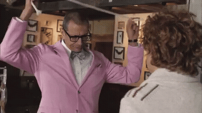 A Man In A Pink Suit And Bow Tie Is Dancing With Another Man . GIF