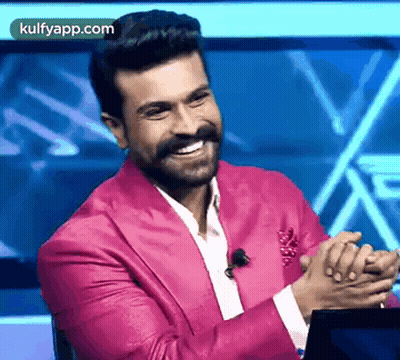 A Man In A Pink Suit Is Sitting In Front Of A Laptop And Smiling . GIF