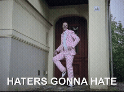 A Man In A Pink Suit Is Standing In Front Of A Door With The Words Haters Gonna Hate Written Below Him GIF