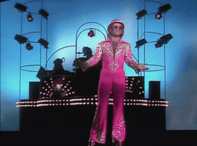 A Man In A Pink Suit Is Standing In Front Of A Stage GIF