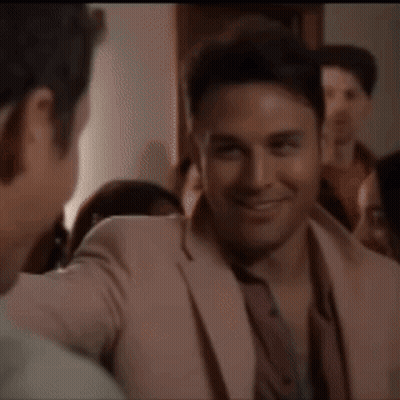 A Man In A Pink Suit Is Talking To Another Man In A Crowd GIF
