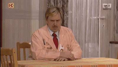 A Man In A Pink Suit Sits At A Table With A Tennis Ball On The Wall Above Him That Says Op12 GIF