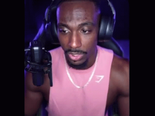 A Man In A Pink Tank Top And Headphones Is Talking Into A Microphone . GIF
