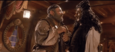A Man In A Pirate Costume Talks To Another Man In A White Dress GIF