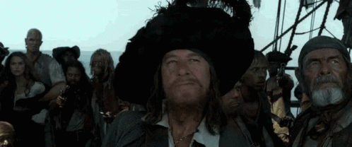 A Man In A Pirate Hat Stands In Front Of A Group Of Men GIF
