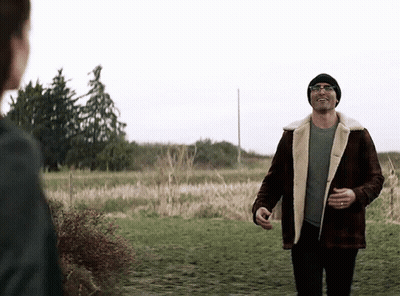 A Man In A Plaid Jacket And A Beanie Is Walking In A Field . GIF