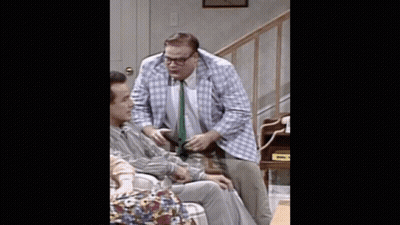 A Man In A Plaid Jacket And Tie Is Talking To Another Man In A Chair GIF