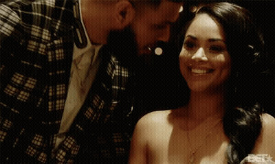 A Man In A Plaid Jacket Kisses A Smiling Woman On The Forehead GIF