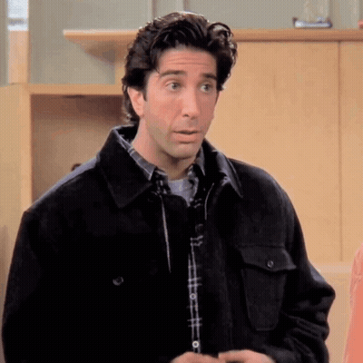 A Man In A Plaid Shirt And A Black Jacket Is Standing In A Room . GIF