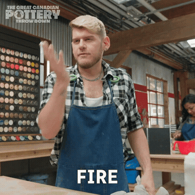 A Man In A Plaid Shirt And Apron Is Making A Fire Gesture GIF