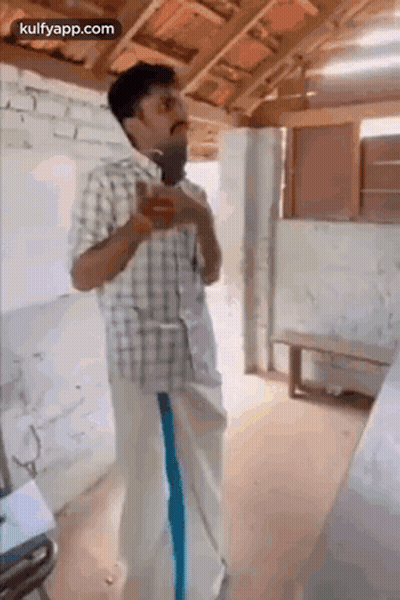 A Man In A Plaid Shirt And Blue Pants Is Standing In A Room With A Microphone In His Hand . GIF
