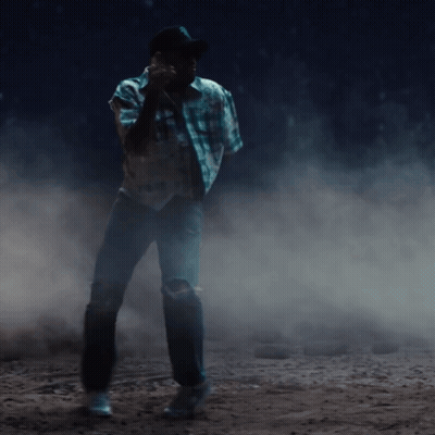 A Man In A Plaid Shirt And Cowboy Hat Is Standing In A Dark Room GIF