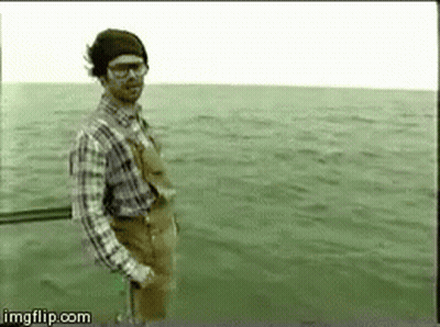 A Man In A Plaid Shirt And Overalls Is Standing In The Water . GIF