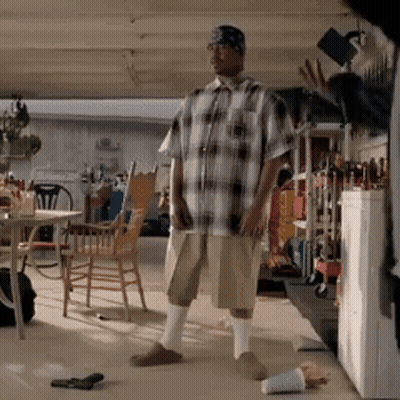 A Man In A Plaid Shirt And Shorts Is Standing In A Garage GIF