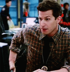A Man In A Plaid Shirt And Tie Has A Badge Around His Neck GIF