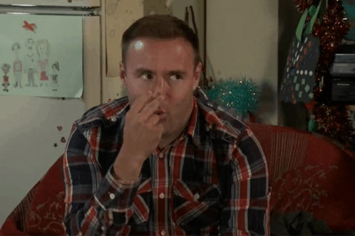 A Man In A Plaid Shirt Holds His Nose GIF