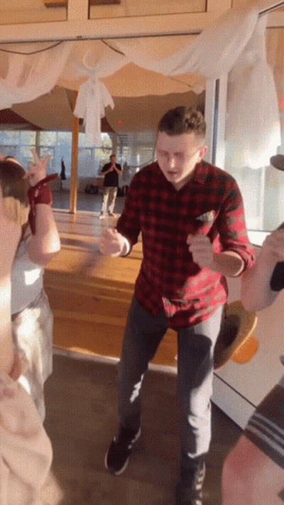 A Man In A Plaid Shirt Is Dancing In Front Of A Window GIF
