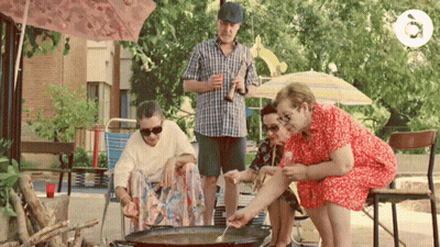 A Man In A Plaid Shirt Is Holding A Bottle Of Beer While A Group Of People Sit Around A Pan GIF