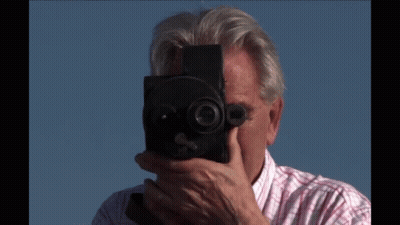 A Man In A Plaid Shirt Is Holding A Camera GIF