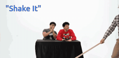 A Man In A Plaid Shirt Is Holding A Cane In Front Of A Chalkboard That Says Shake It GIF