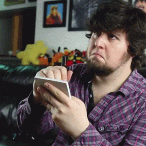 A Man In A Plaid Shirt Is Holding A Cell Phone And Making A Face GIF