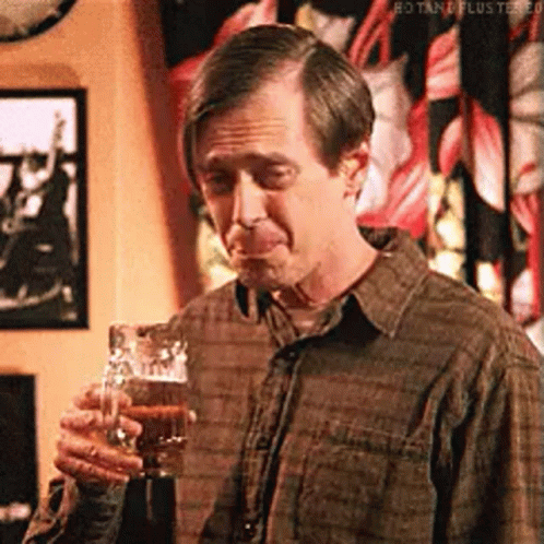 A Man In A Plaid Shirt Is Holding A Glass Of Beer And Making A Funny Face . GIF