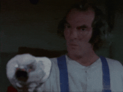 A Man In A Plaid Shirt Is Holding A Gun In His Hand . GIF