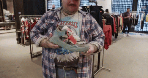 A Man In A Plaid Shirt Is Holding A Pair Of Shoes In His Hands GIF