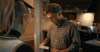 A Man In A Plaid Shirt Is Holding An Apple Product In His Hand GIF