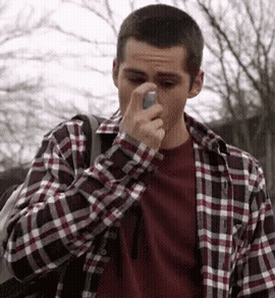 A Man In A Plaid Shirt Is Holding An Asthma Inhaler To His Nose . GIF
