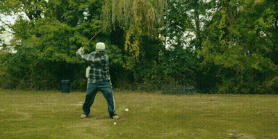 A Man In A Plaid Shirt Is Jumping In The Air In A Park GIF