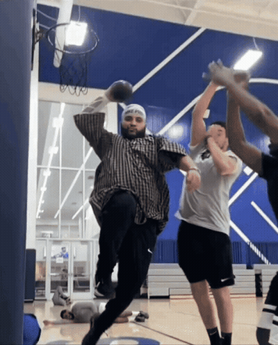 A Man In A Plaid Shirt Is Jumping In The Air With A Basketball In His Hand GIF