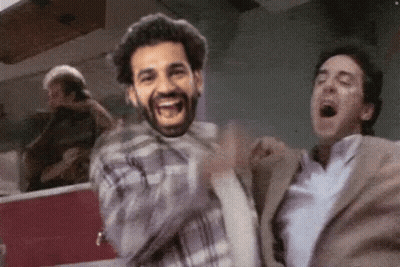A Man In A Plaid Shirt Is Laughing While Another Man In A Suit Is Yawning . GIF