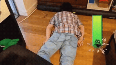 A Man In A Plaid Shirt Is Laying On The Floor Next To A Green Frog GIF