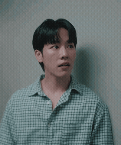 a man in a plaid shirt is leaning against a white wall