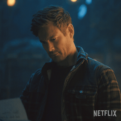 A Man In A Plaid Shirt Is Looking At A Piece Of Paper With Netflix Written On The Bottom GIF
