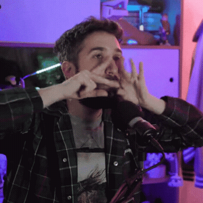 A Man In A Plaid Shirt Is Making A Face With His Hands In Front Of A Microphone GIF