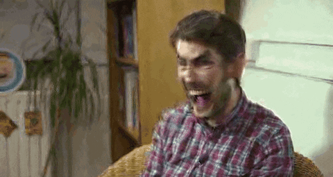 A Man In A Plaid Shirt Is Making A Funny Face While Sitting In A Chair . GIF