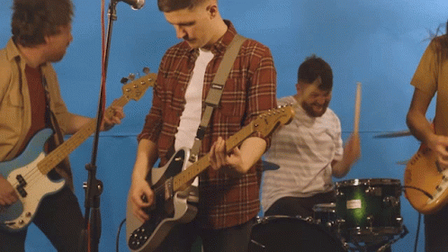 A Man In A Plaid Shirt Is Playing A Guitar In Front Of A Drum Set GIF