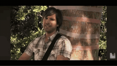 A Man In A Plaid Shirt Is Playing A Guitar In Front Of A Tree . GIF