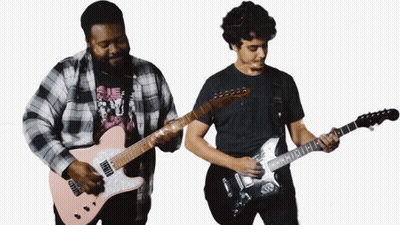 A Man In A Plaid Shirt Is Playing A Guitar Next To Another Man GIF