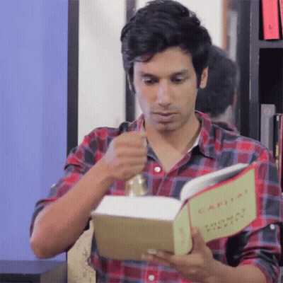 A Man In A Plaid Shirt Is Reading The Book Capital GIF