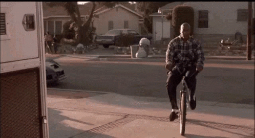 A Man In A Plaid Shirt Is Riding A Bike Down The Street GIF