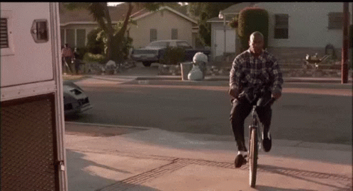 A Man In A Plaid Shirt Is Riding A Bike On A Sidewalk GIF