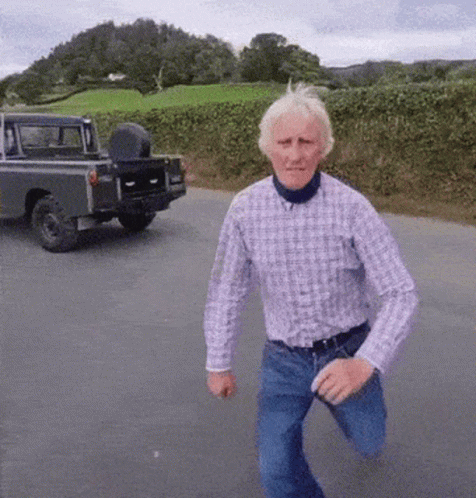 A Man In A Plaid Shirt Is Running Down A Road In Front Of A Truck GIF