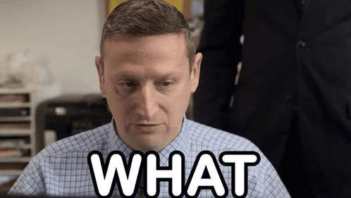 A Man In A Plaid Shirt Is Sitting At A Desk And Says What GIF